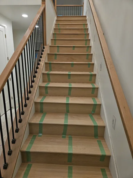 Tape keeps the stair nosing and planks fitted tightly together as the glue sets. This view shows the fitted edges alongside the railing.